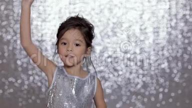 可爱快乐的小女孩穿着银色的裙子在银色的背景下跳舞。